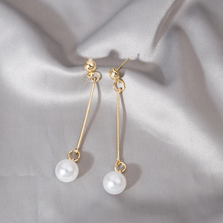 Goldene Ohrringe mit Perlenanhänger auf grauem Seidenstoff, eleganter Schmuck, Damenaccessoire.