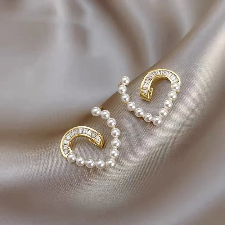 Goldene Ohrringe mit Perlen und Kristallen auf Seidenstoff, eleganter Schmuck, luxuriöses Design.