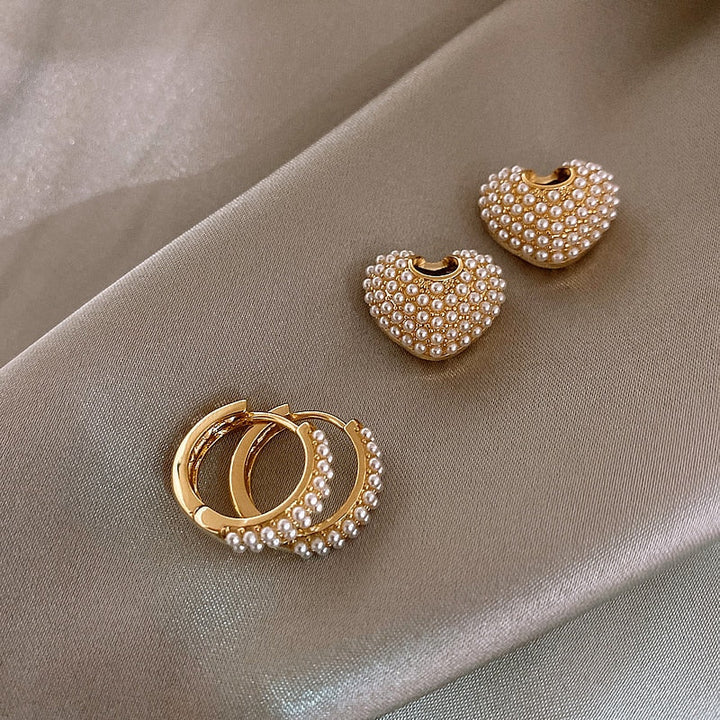 Goldene Ohrringe mit Perlen, Herzform und Creolen, eleganter Schmuck auf Seidenstoff.