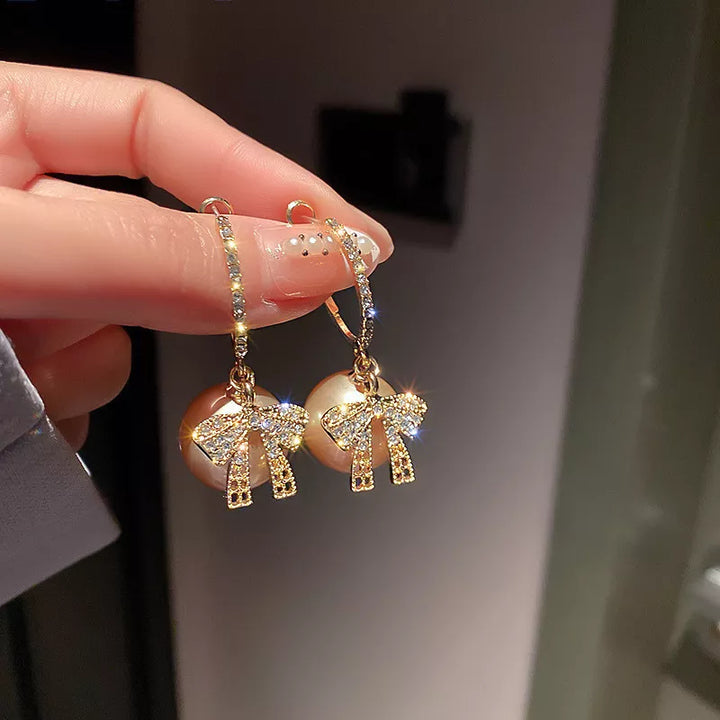 Goldene Ohrringe mit Perlen und Schleifen, funkelnde Strasssteine, eleganter Schmuck.