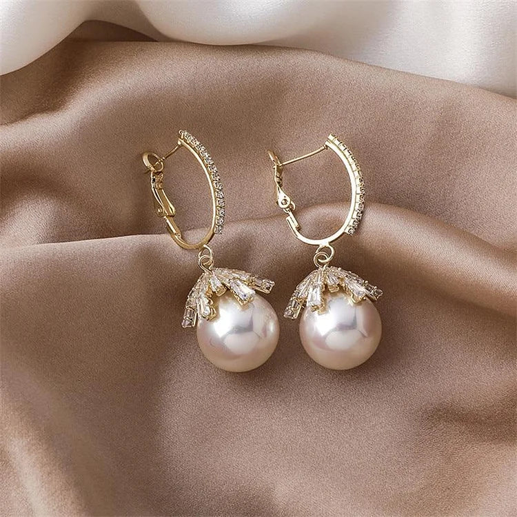 Goldene Ohrringe mit Perlen und Strasssteinen auf beigem Stoff, eleganter Schmuck für Damen.
