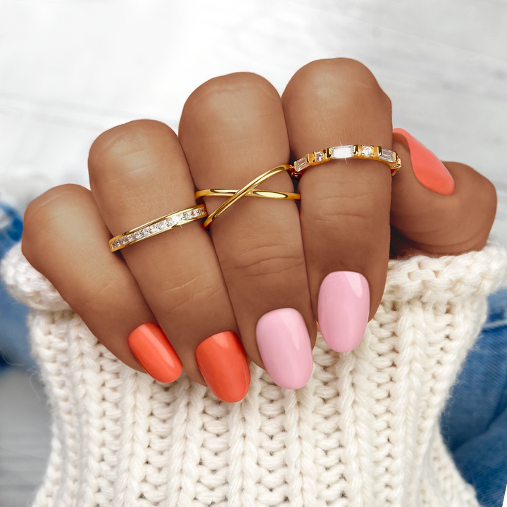 Vier goldene Ringe an Hand mit orange und rosa Nägeln, gestrickter Pullover, modisch.