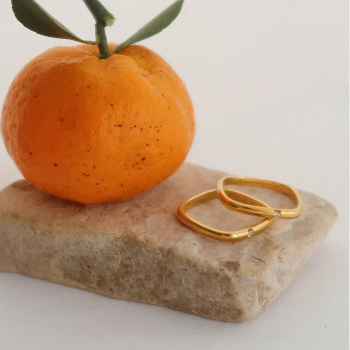Goldene Ringe mit Diamanten auf Stein neben Mandarine, Schmuck, minimalistisch, elegant.