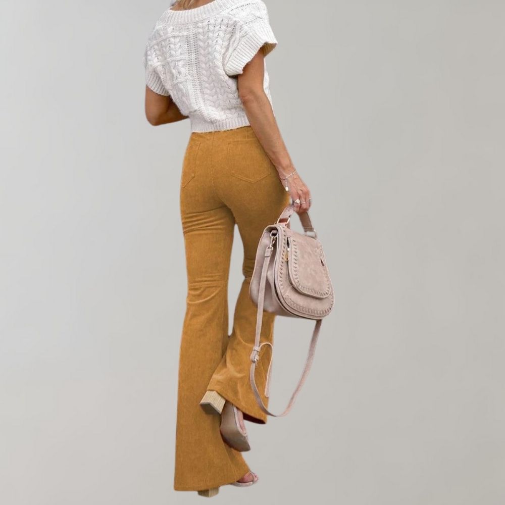 Frau in weißem Strickoberteil und goldener Schlaghose mit beiger Handtasche.
