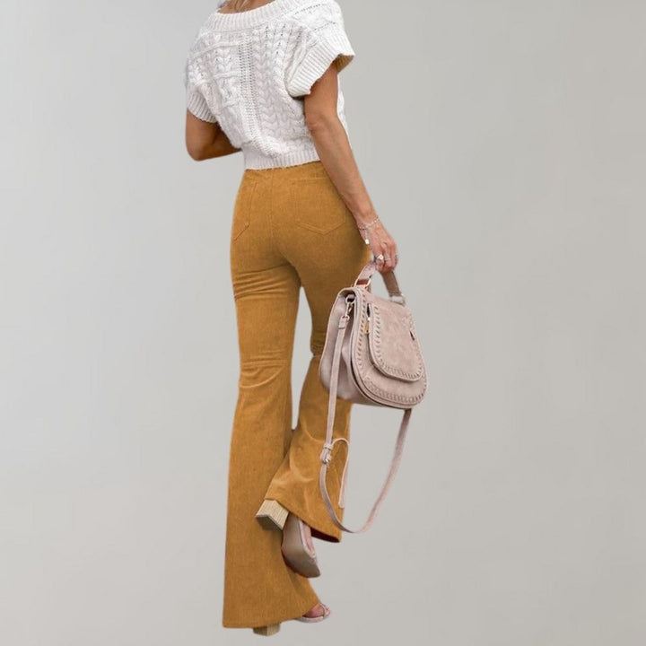 Frau in weißem Strickoberteil und goldener Schlaghose mit beiger Handtasche.