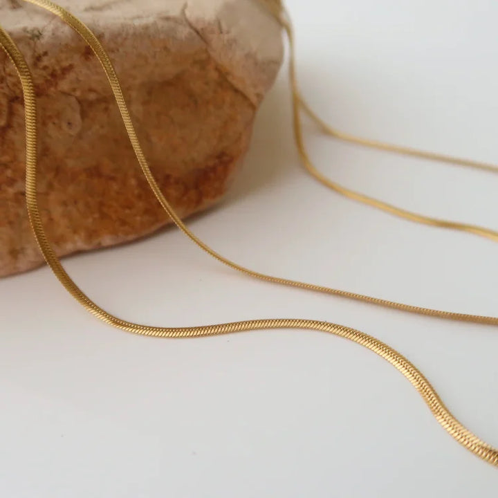 Goldene Schlangenkette auf Stein, elegantes Schmuckdesign, modisches Accessoire, Damenhalskette.