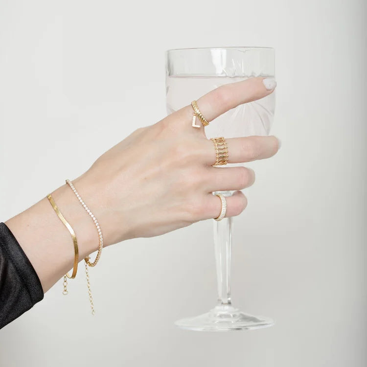 Hand mit goldenen Ringen und Armbändern hält Weinglas, Schmuck, Modeaccessoires, elegantes Design.