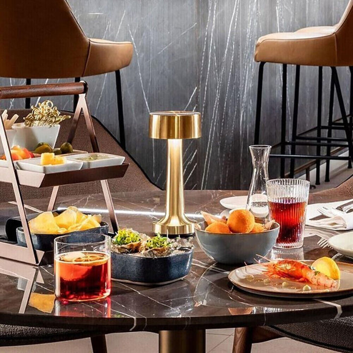 Goldene Tischlampe auf Marmortisch mit Snacks und Getränken in modernem Restaurantumfeld.