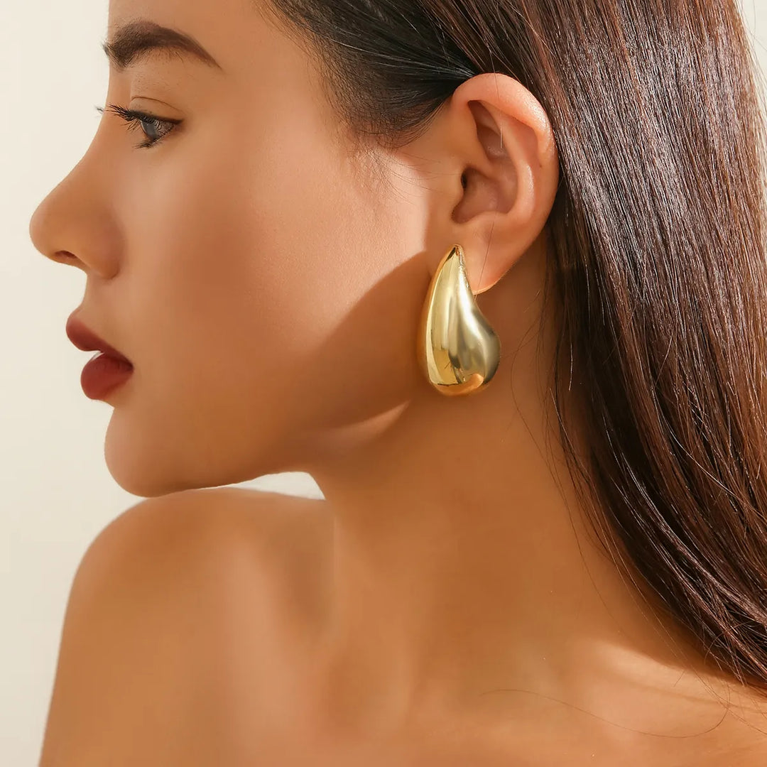 Frau mit goldenen Tropfen-Ohrringen, eleganter Schmuck, Modeaccessoire, Nahaufnahme.