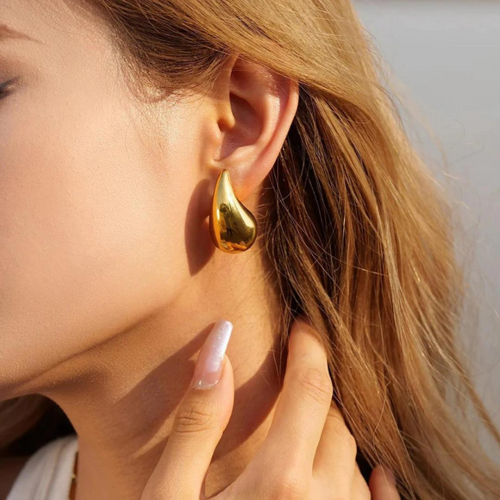 Frau mit goldenen Tropfen-Ohrringen, Nahaufnahme, eleganter Schmuck, modisches Accessoire.
