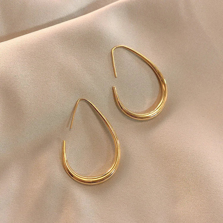 Goldene Tropfen-Ohrringe auf beigem Stoff, eleganter Schmuck, modisches Accessoire.