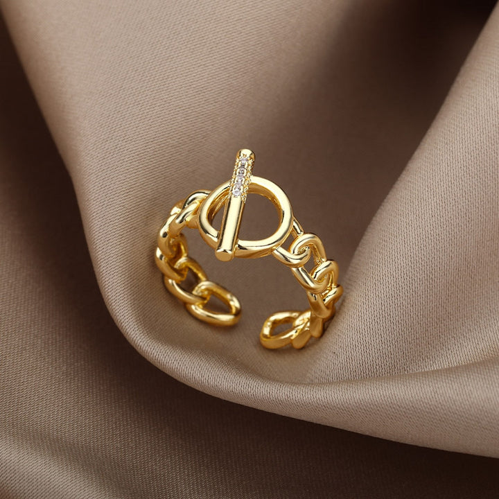 Goldener Ring mit Kettendesign und Zirkonia, modisches Schmuckstück auf beigem Stoff.