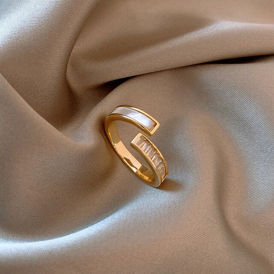 Goldener Ring mit Perlmutt- und Kristalleinlage auf beigem Stoff, elegantes Schmuckdesign.