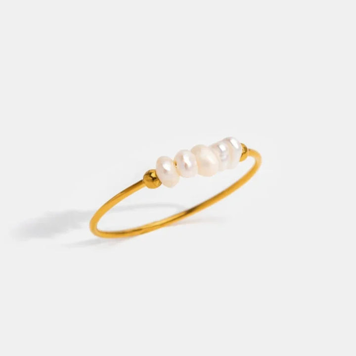 Goldener Armreif mit weißen Perlen, elegantes Schmuckstück, minimalistisches Design.
