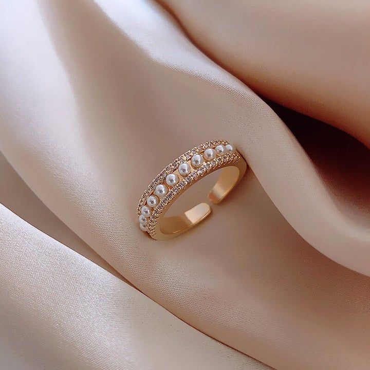 Goldener Ring mit Perlen und Strasssteinen auf beigem Stoff, eleganter Schmuck, Damenaccessoire.