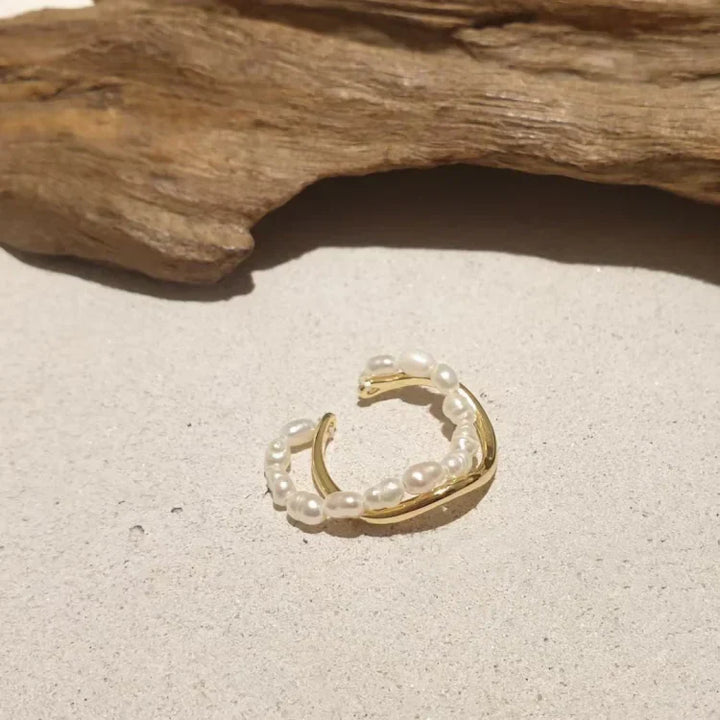 Goldener Ring mit Perlen, Schmuck, elegantes Design, auf Sand mit Holz im Hintergrund.