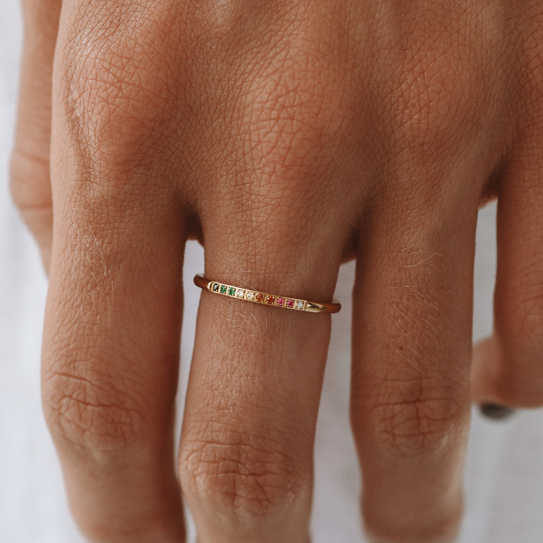 Goldener Regenbogenring mit bunten Edelsteinen auf Hand getragen.