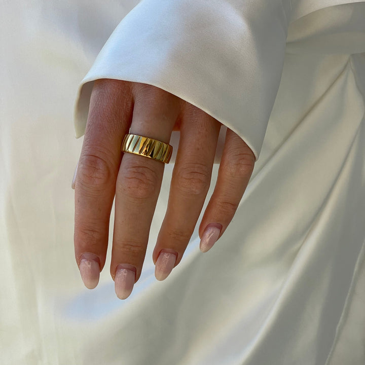 Goldener Ring an Hand mit weißem Seidenhemd, elegantes Schmuckdesign, Damenmode Accessoire.