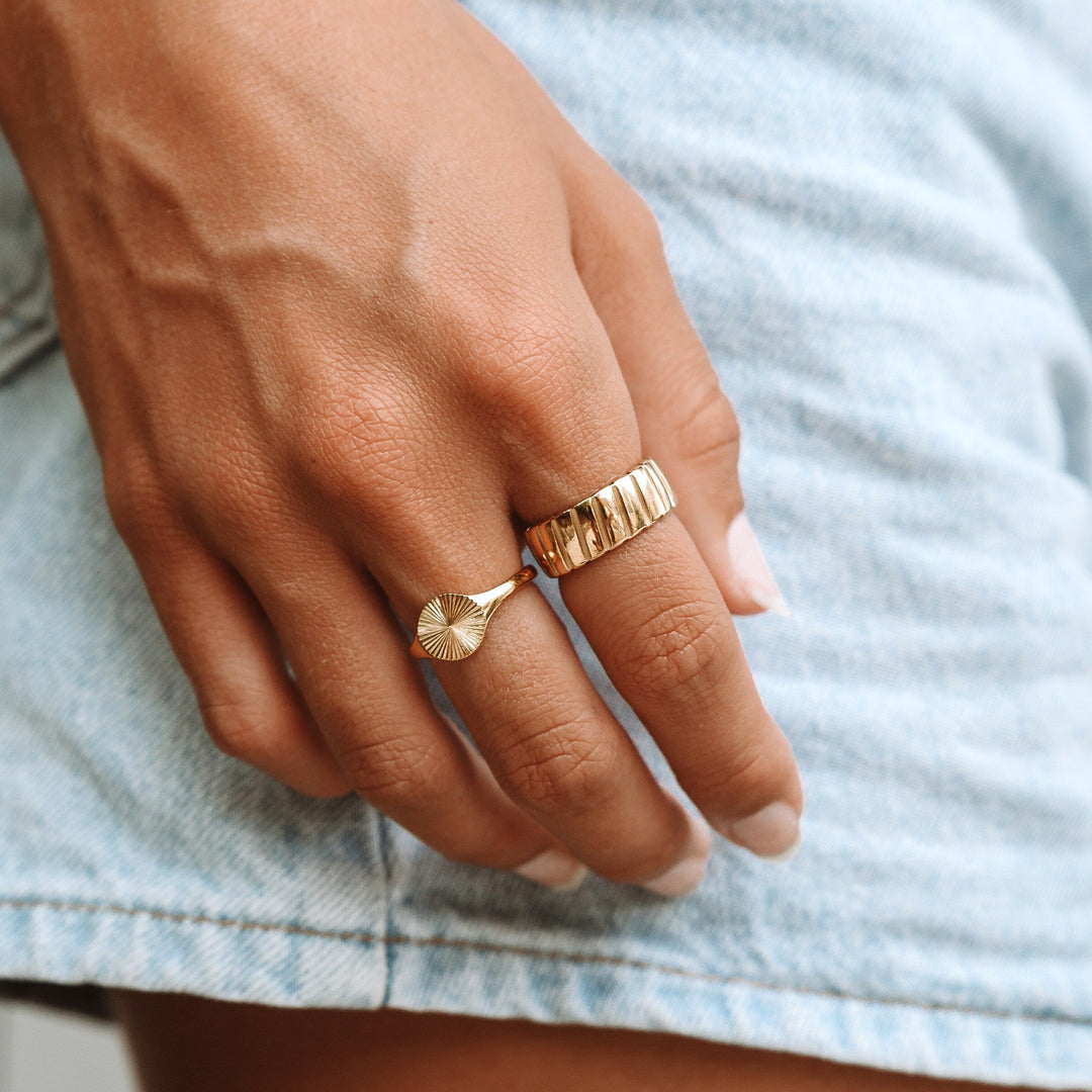 Goldene Ringe an Hand, einer mit Rillenmuster, auf Jeanshintergrund.