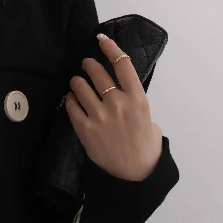 Hand mit goldenen Ringen hält schwarze Lederhandtasche, elegantes Accessoire, Damenmode.