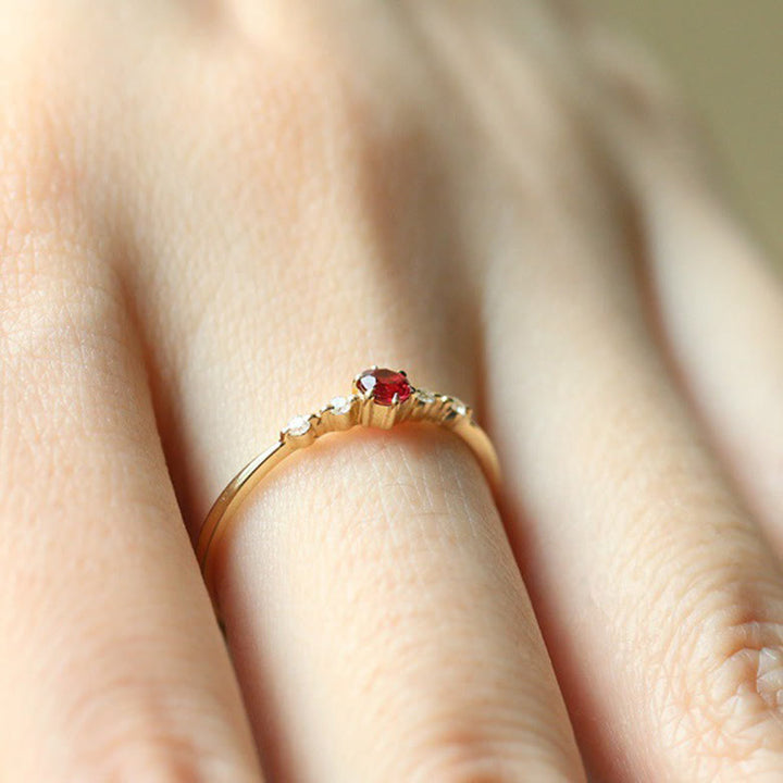 Goldener Ring mit rotem Edelstein und Diamanten auf Hand, eleganter Schmuck, Verlobungsring.