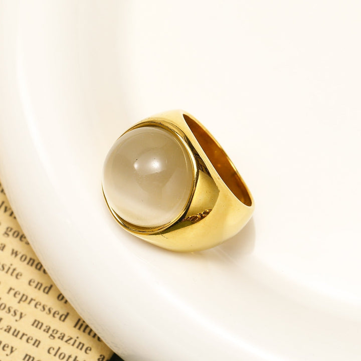 Goldener Ring mit großem, rundem Mondstein auf weißem Hintergrund, elegantes Schmuckdesign.