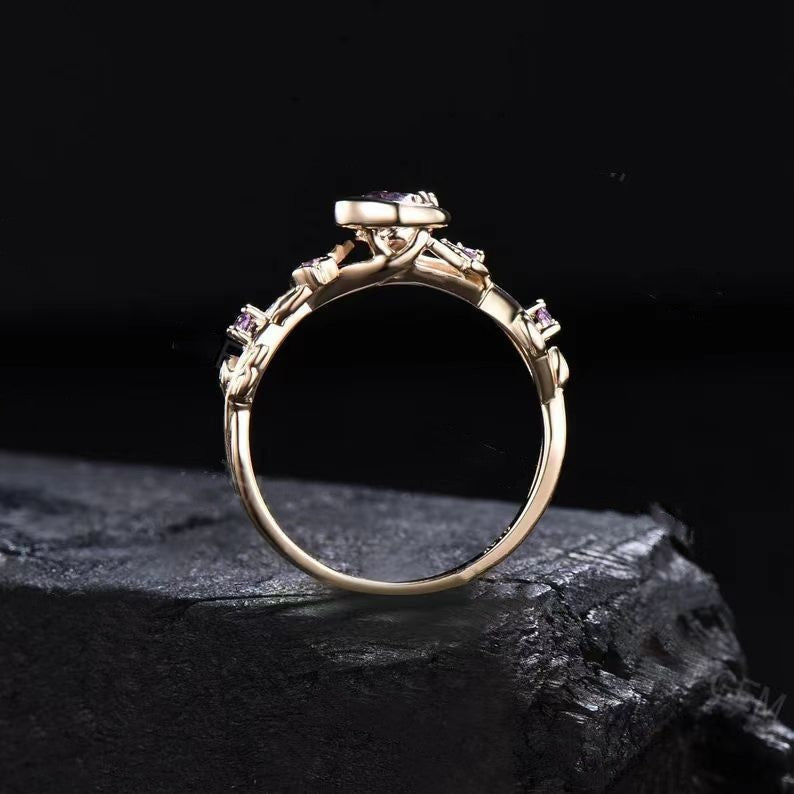 Goldener Verlobungsring mit violettem Edelstein, filigranes Design, auf schwarzem Hintergrund.