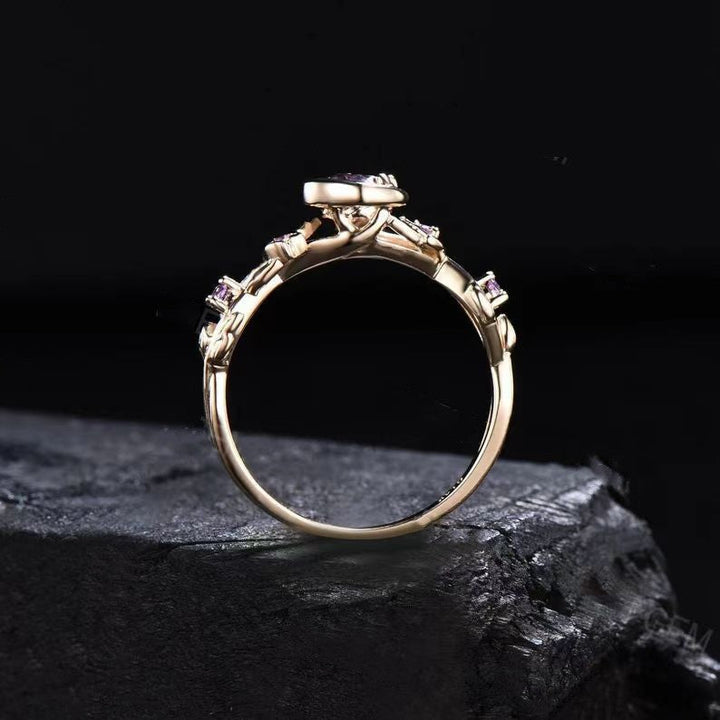 Goldener Verlobungsring mit violettem Edelstein, filigranes Design, auf schwarzem Hintergrund.