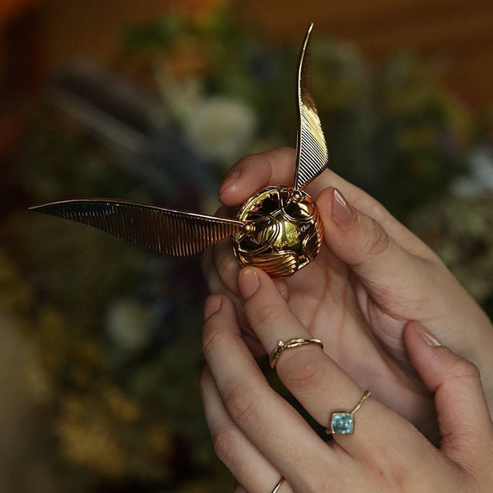 Goldener Schnatz Deko-Objekt, metallisch, detailreich, in Händen gehalten, Harry Potter Fanartikel.