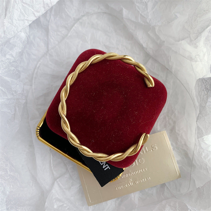 Goldener Twist-Armreif aus Edelstahl auf rotem Samtkissen, elegantes Schmuckdesign.