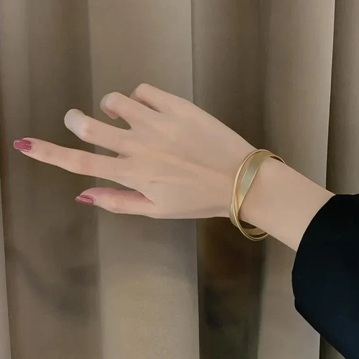 Goldenes Armband am Handgelenk einer Person vor beigem Hintergrund, eleganter Schmuck.