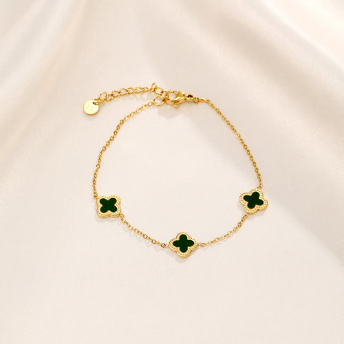 Goldenes Armband mit grünen Kleeblatt-Anhängern auf cremefarbenem Hintergrund.