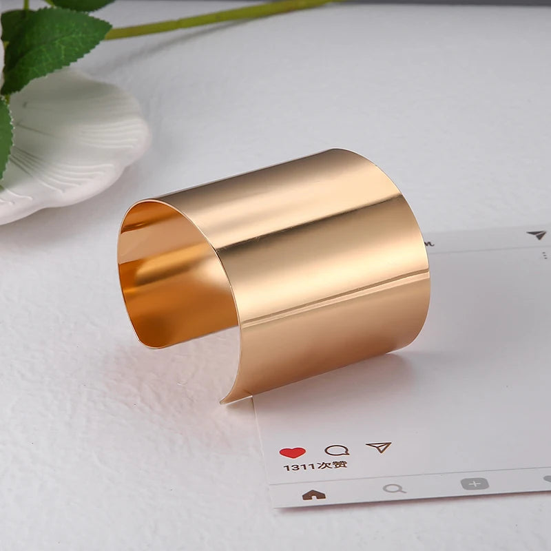 Goldenes Armreif aus Metall, minimalistisches Design, auf weißem Hintergrund.