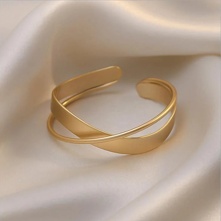 Goldenes Armreif aus Edelstahl auf Seidenstoff, elegantes Schmuckdesign, modisches Accessoire.