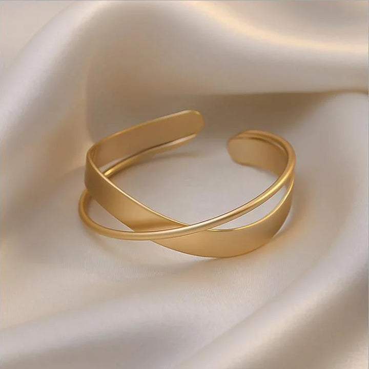 Goldenes Armreif aus Edelstahl auf Seidenstoff, elegantes Schmuckdesign, modisches Accessoire.