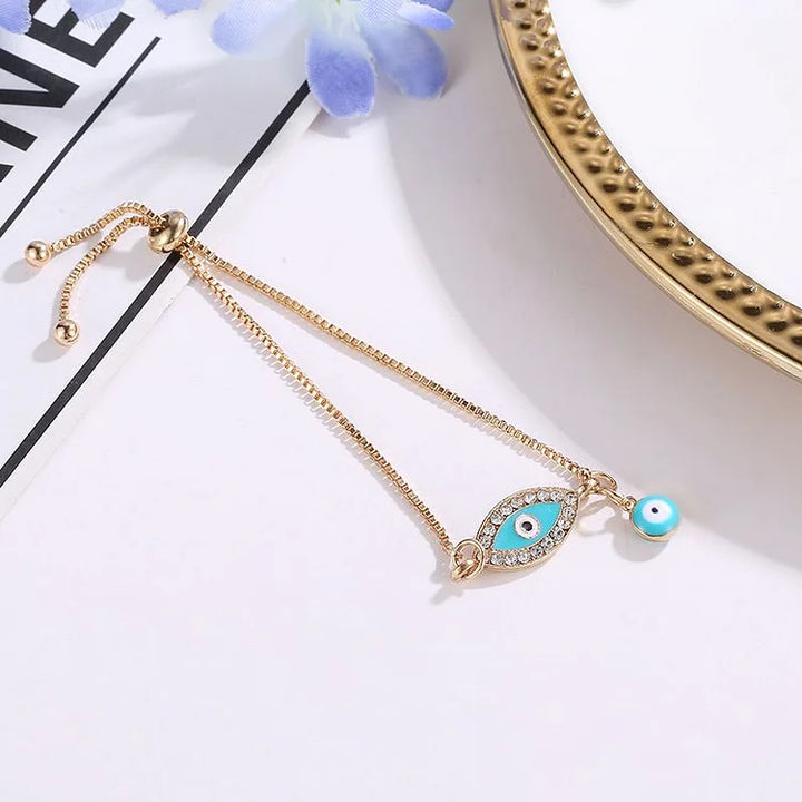Goldenes Armband mit Nazar-Amulett und blauem Anhänger auf weißem Hintergrund, Schmuckdesign.
