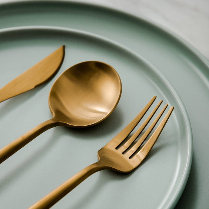 Goldenes Besteck-Set auf mintgrünem Teller, modernes Design, Edelstahl, Essbesteck.