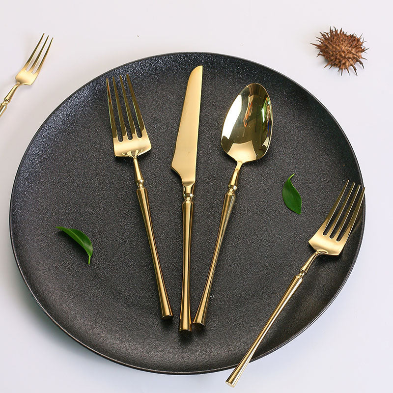 Goldenes Besteckset auf schwarzem Teller, bestehend aus Gabel, Messer, Löffel, elegant, modern.