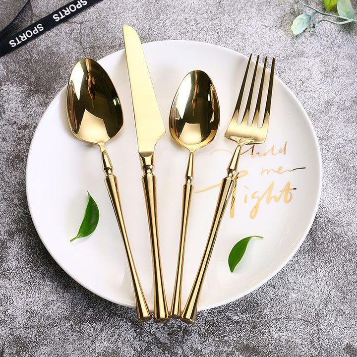 Goldenes Besteckset auf weißem Teller, bestehend aus Messer, Gabel, Löffel und Teelöffel.