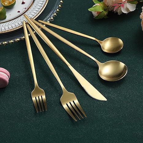 Goldenes Besteckset aus Edelstahl, bestehend aus Gabeln, Löffeln und Messer auf grünem Tuch.