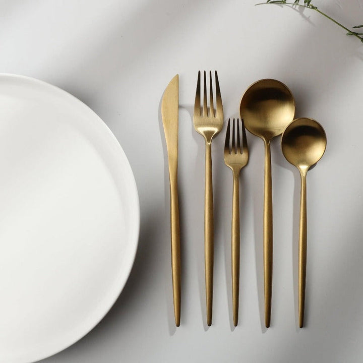 Goldenes minimalistisches Besteck-Set auf weißem Hintergrund, bestehend aus Messer, Gabel, Löffel.