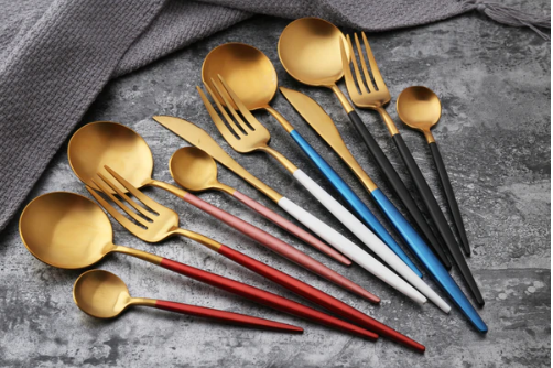 Goldenes Besteckset mit bunten Griffen auf grauem Hintergrund, modernes Design, Edelstahl.