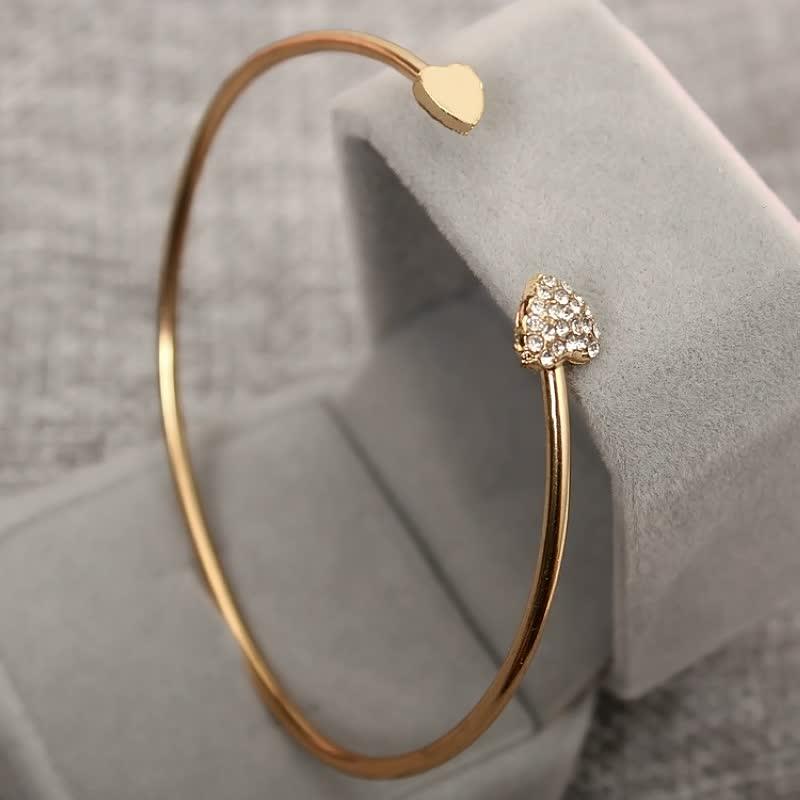 Goldenes Armreif mit Herzdesign und Strasssteinen auf grauem Hintergrund, eleganter Schmuck.