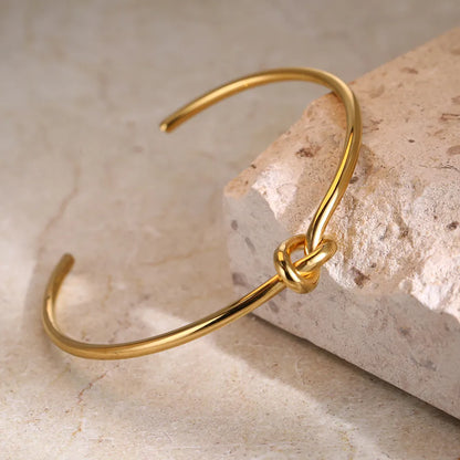Goldenes Armreif mit Knoten-Design auf Stein, eleganter Schmuck, minimalistischer Stil.