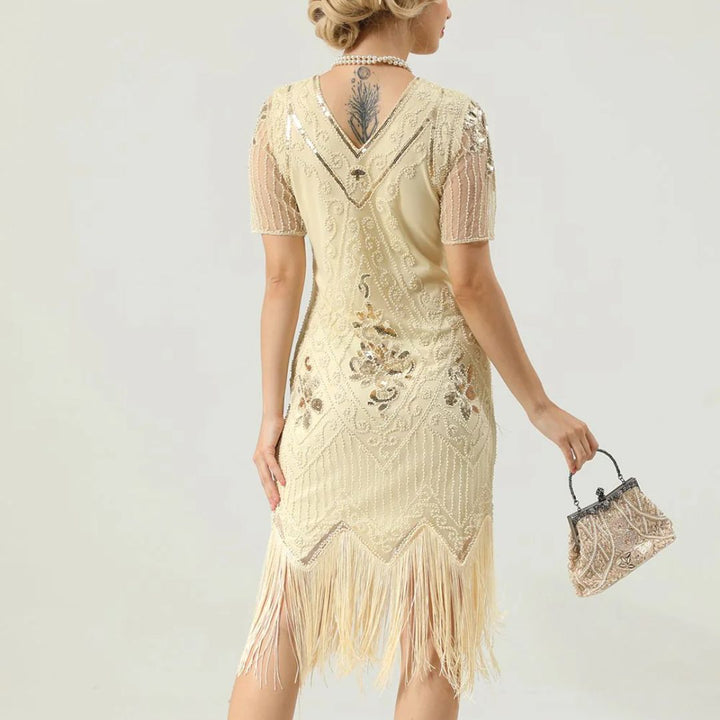 Frau in cremefarbenem Fransen-Kleid mit Pailletten, Vintage-Stil, hält eine kleine Tasche.