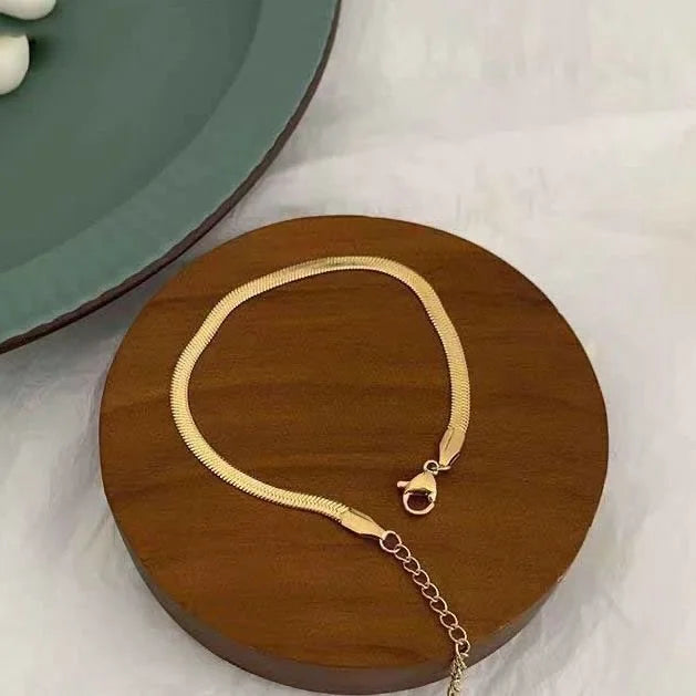 Goldenes Schlangenarmband auf Holzplatte, elegantes Schmuckdesign, Damenaccessoire.