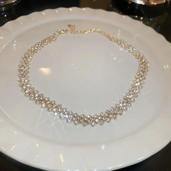 Goldene Halskette mit funkelnden Kristallen auf weißem Teller, eleganter Schmuck für Damen.