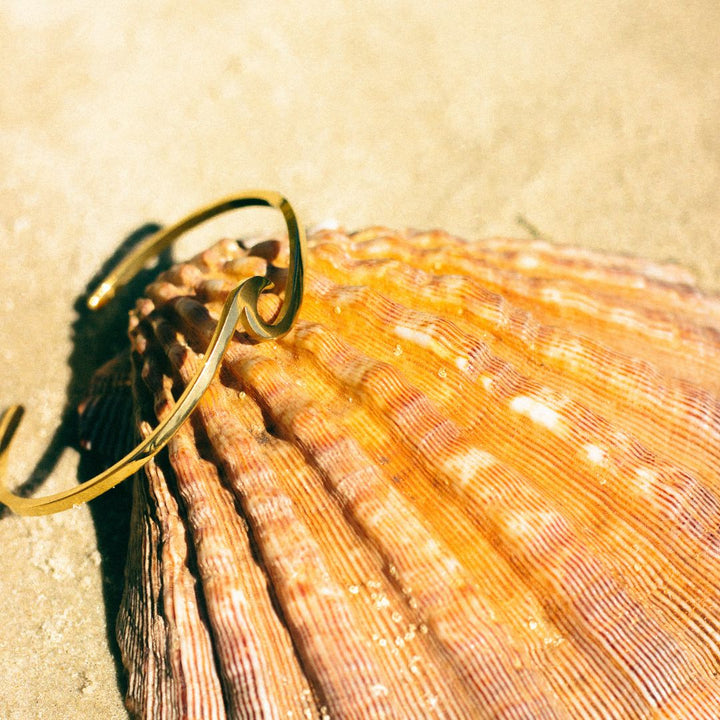 Goldenes Wellenarmband auf Muschel, eleganter Schmuck, Strandmode, Damenaccessoire.