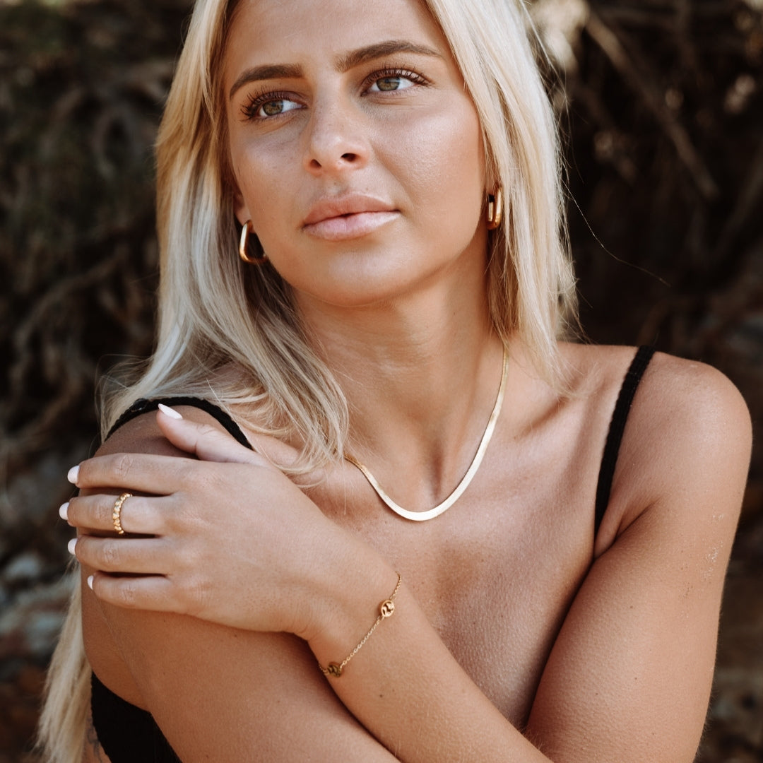 Blonde Frau mit goldener Halskette, Armband und Ohrringen, Sommermode, Strandhintergrund.