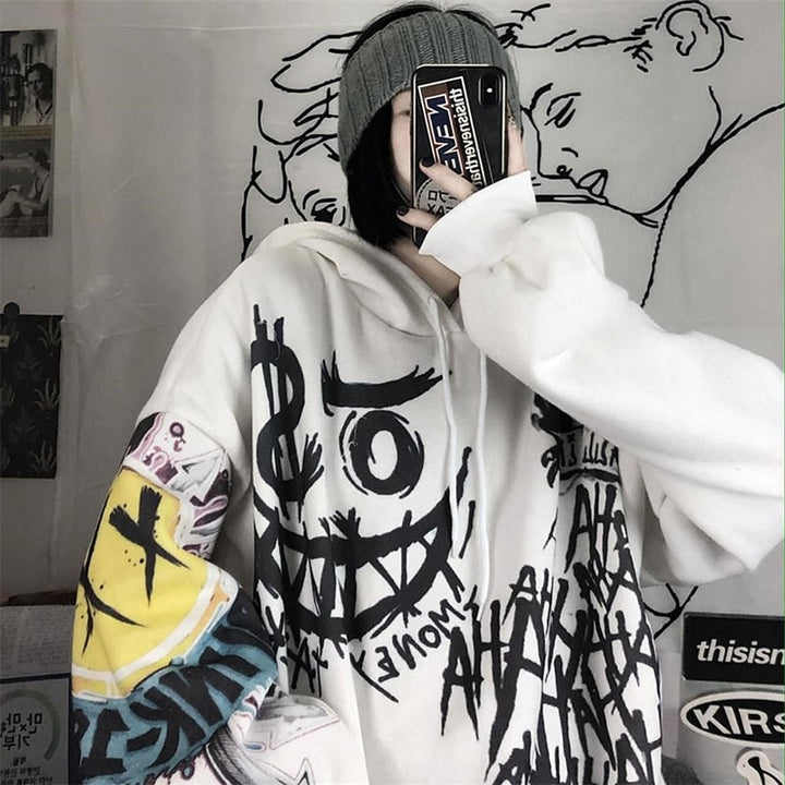 Person in weißem Graffiti-Hoodie mit Smartphone, grauer Mütze, urbaner Streetwear-Look.